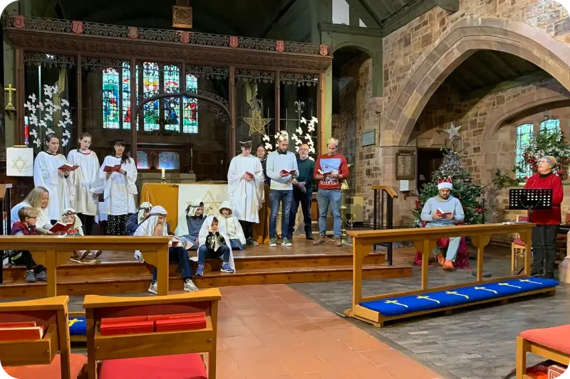 Image of a group of singers standing beside the alter.  Sitting on the floor in front of them are a group of young people dressed as shepherds.