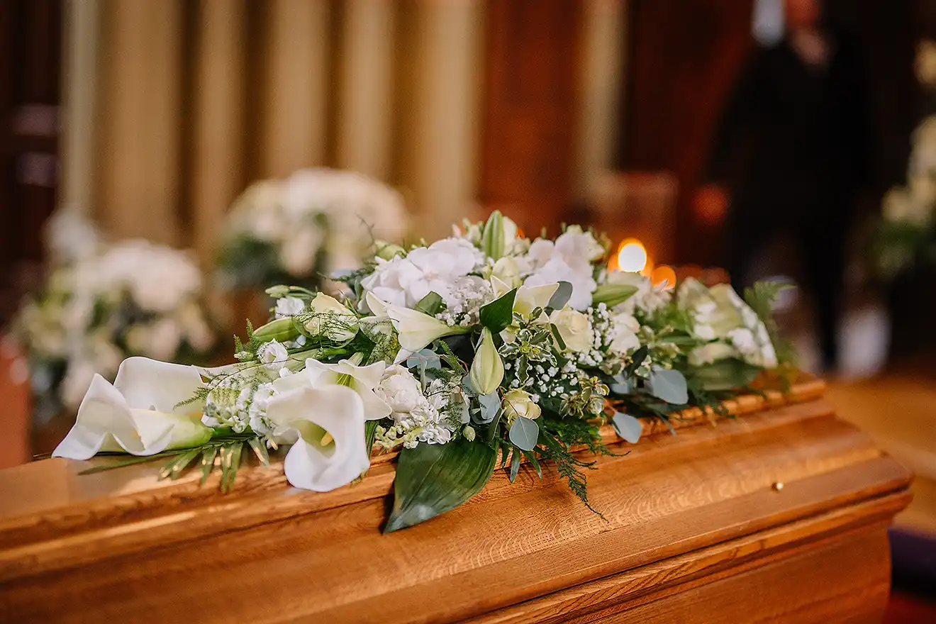A coffin decorated with many flowers and candles in a beautiful church ceremony